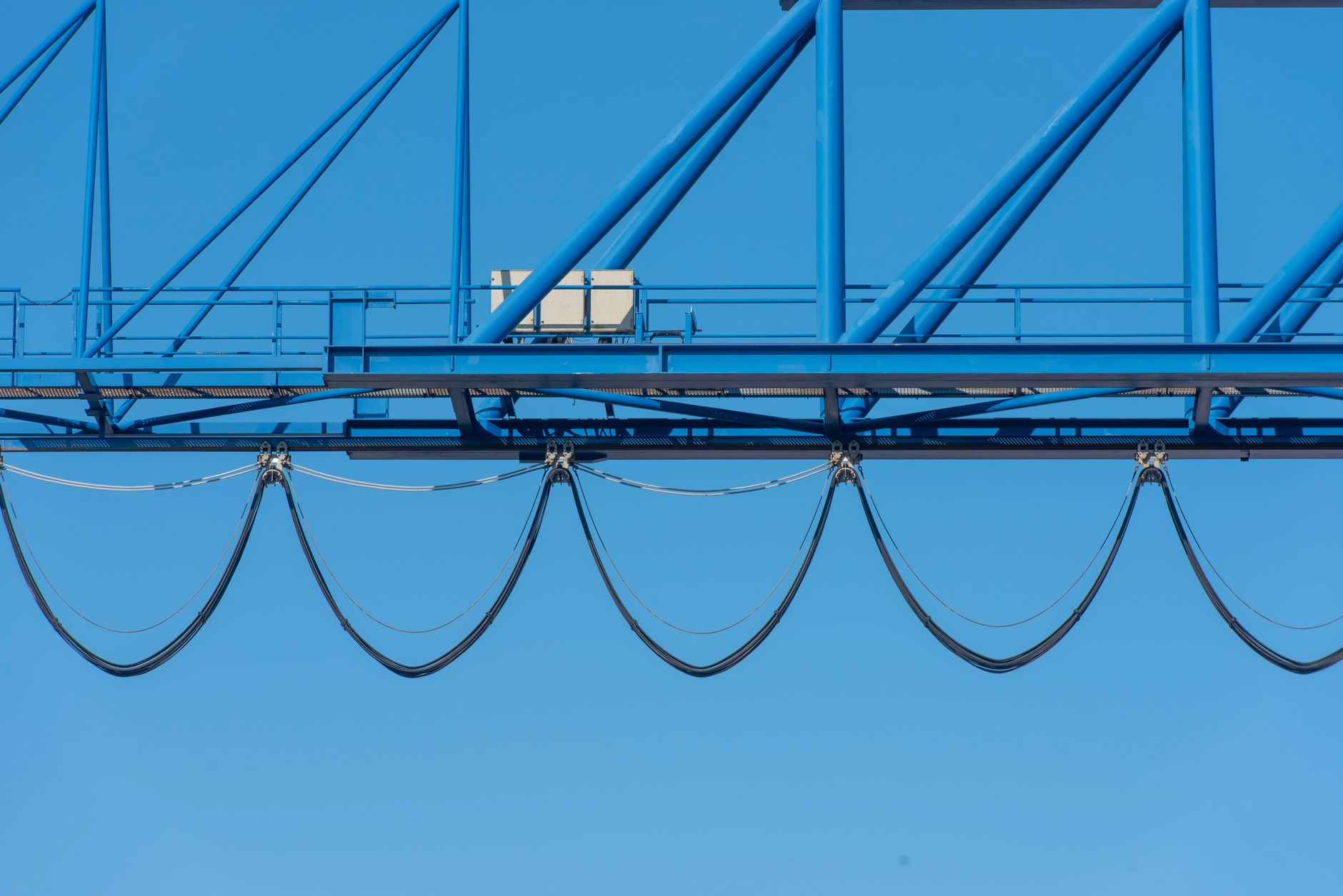 Close-up of a blue industrial crane against a clear blue sky, showcasing structure cables.