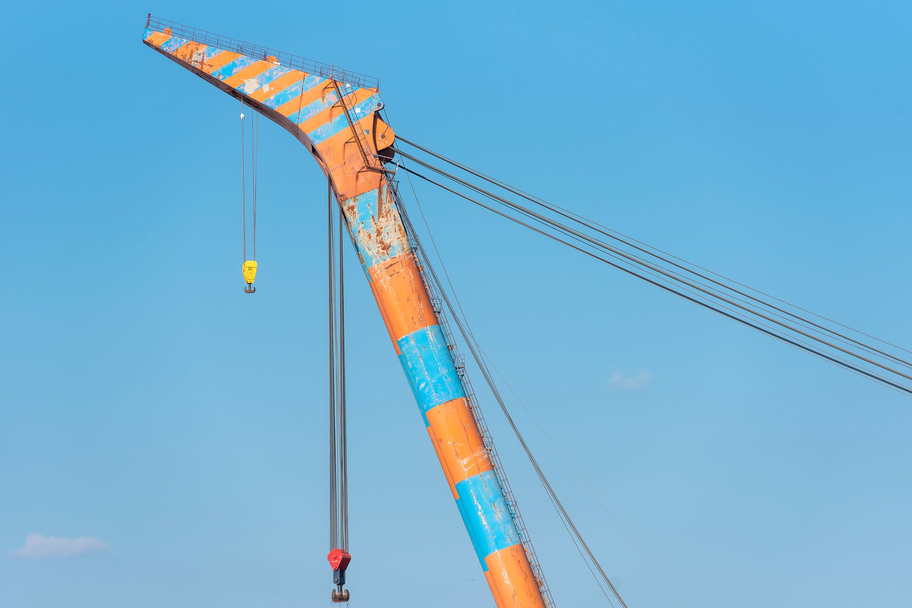 A vibrant orange and blue crane extending into a bright clear sky, displaying industrial strength and color.